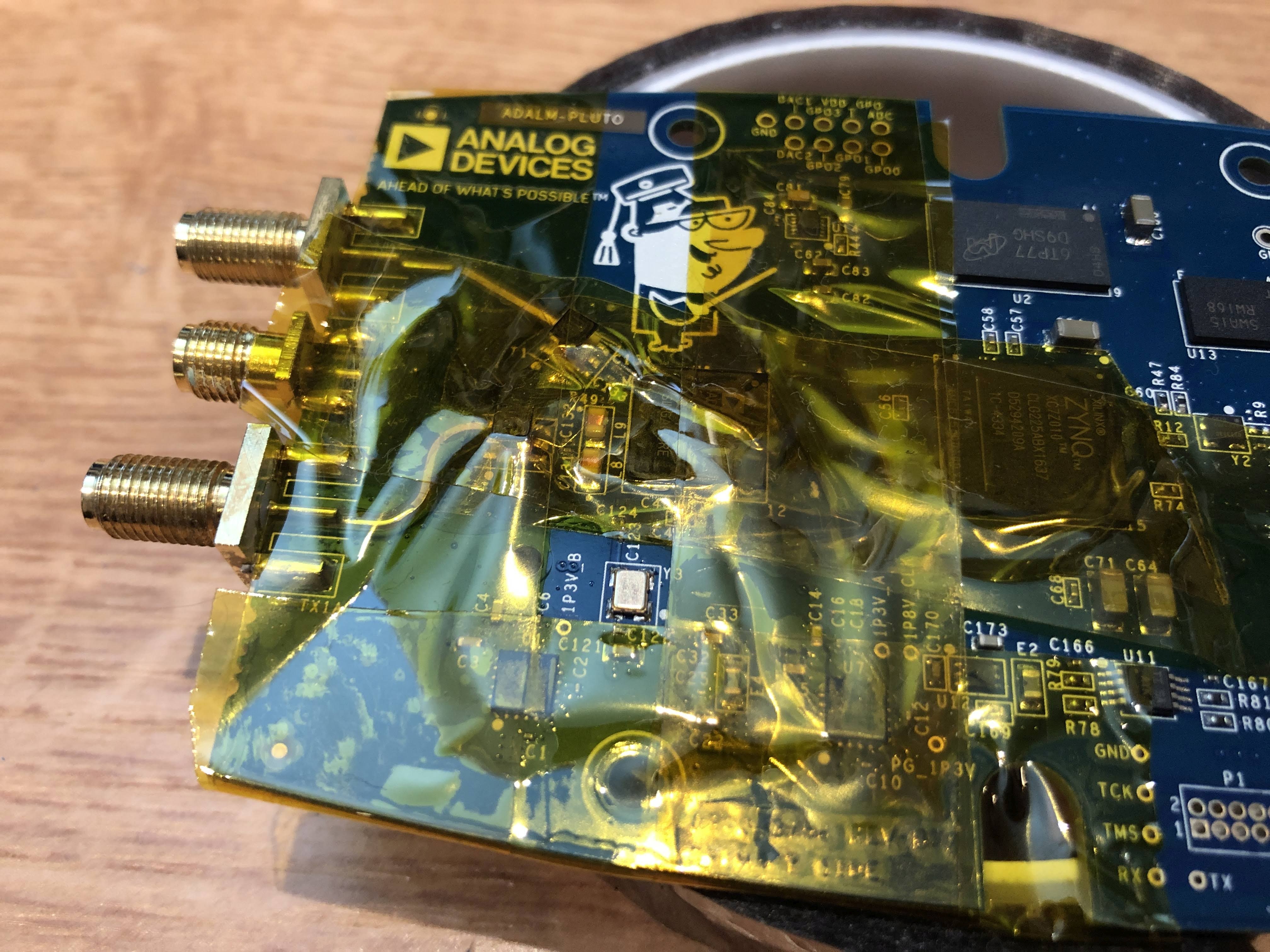 PlutoSDR PCB, most parts masked off with Kapton tape, except for the crystal oscillator